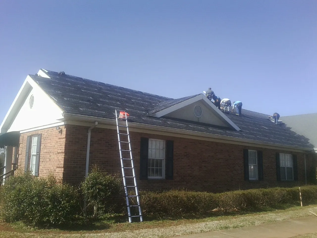Crew tearing shingles off a brick ranch roof with a ladder set — Emergency Roof Repair work by our crew in Rensselaerville