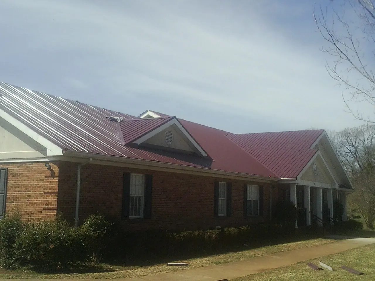 Red metal roof with gabled entries on a long brick building, from a Hail Damage Roof Repair job in Rensselaerville