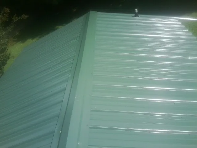 New green metal panels meeting at the ridge of a roof — Flat Roof Repair work by our crew in Rensselaerville