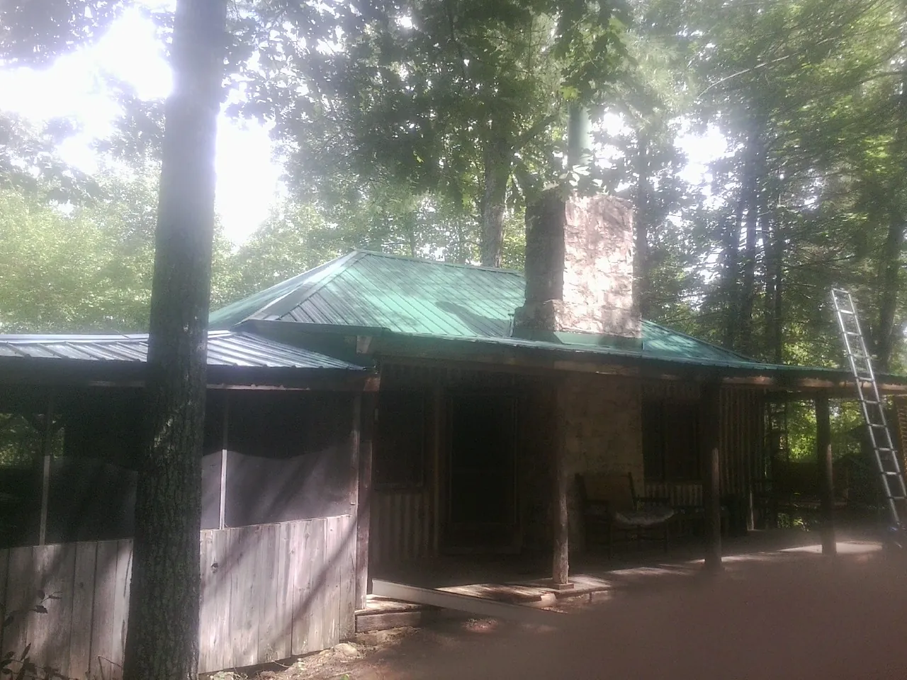 Green metal roof and stone chimney above a log cabin porch in Rensselaerville