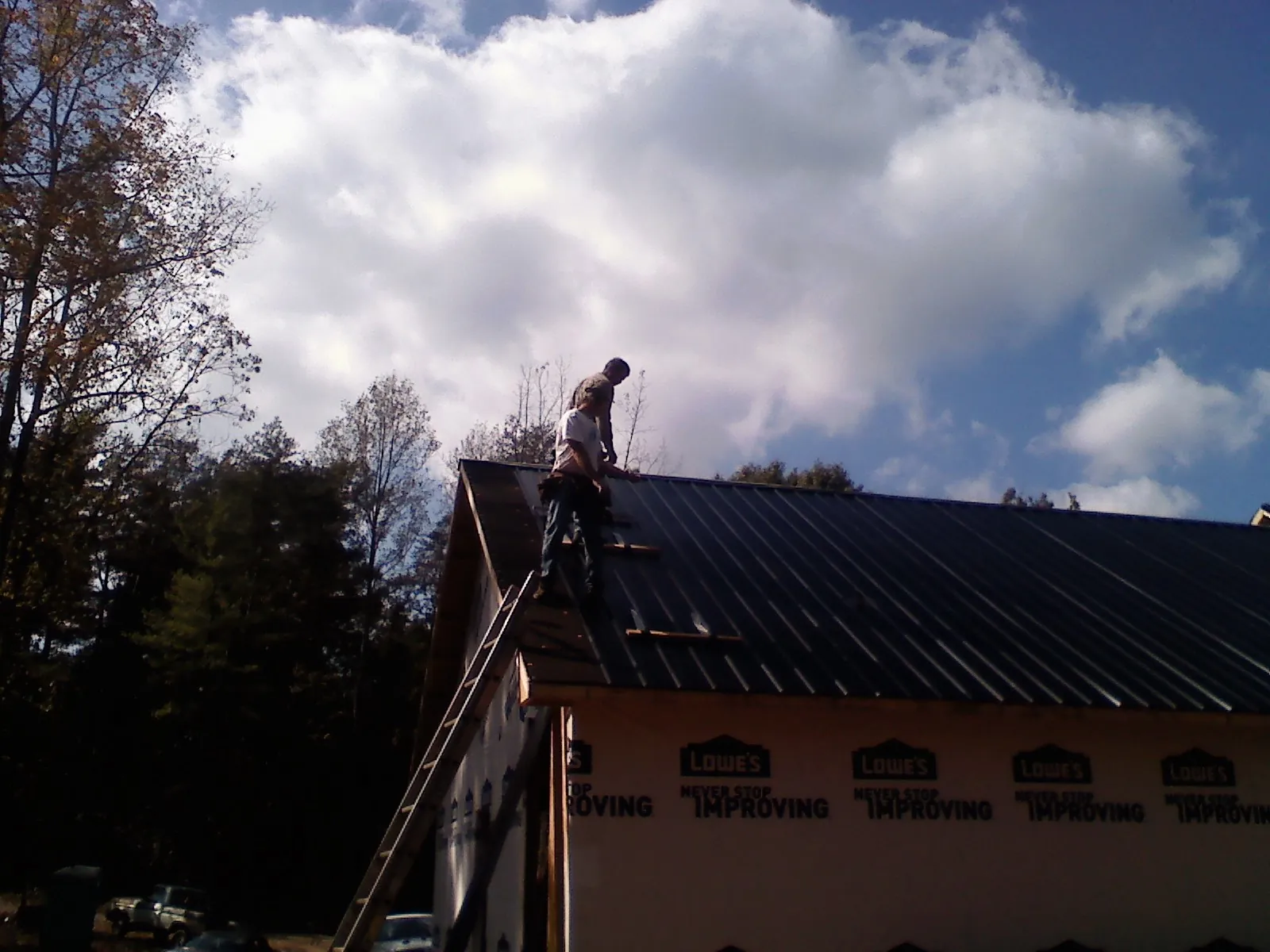 Roofer fastening dark metal panels high against a cloudy sky, from a Roof Inspection job in Rensselaerville