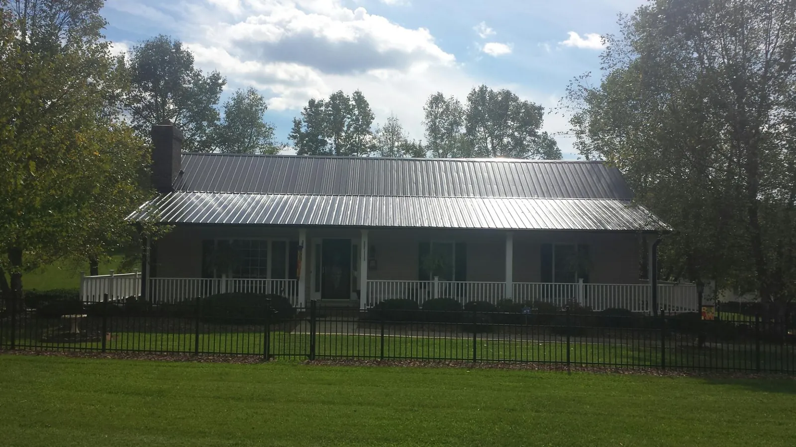 Gray metal roof on a brick ranch with a full width front porch — Gutter Guard Installation work by our crew in Rensselaerville