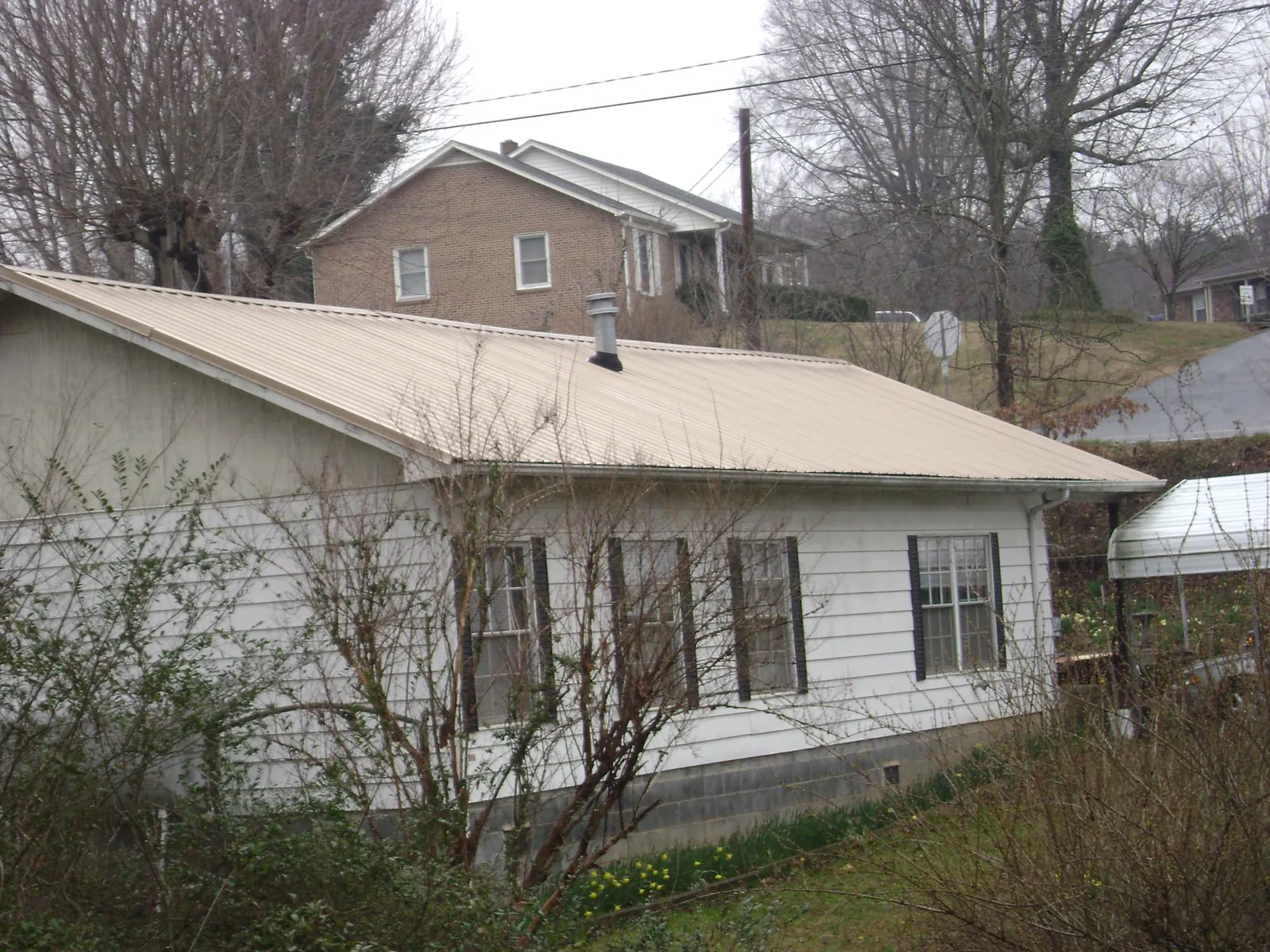 Tan metal roof on a white sided house set into a hillside — Commercial Roofing by Roofing Brothers in Rensselaerville