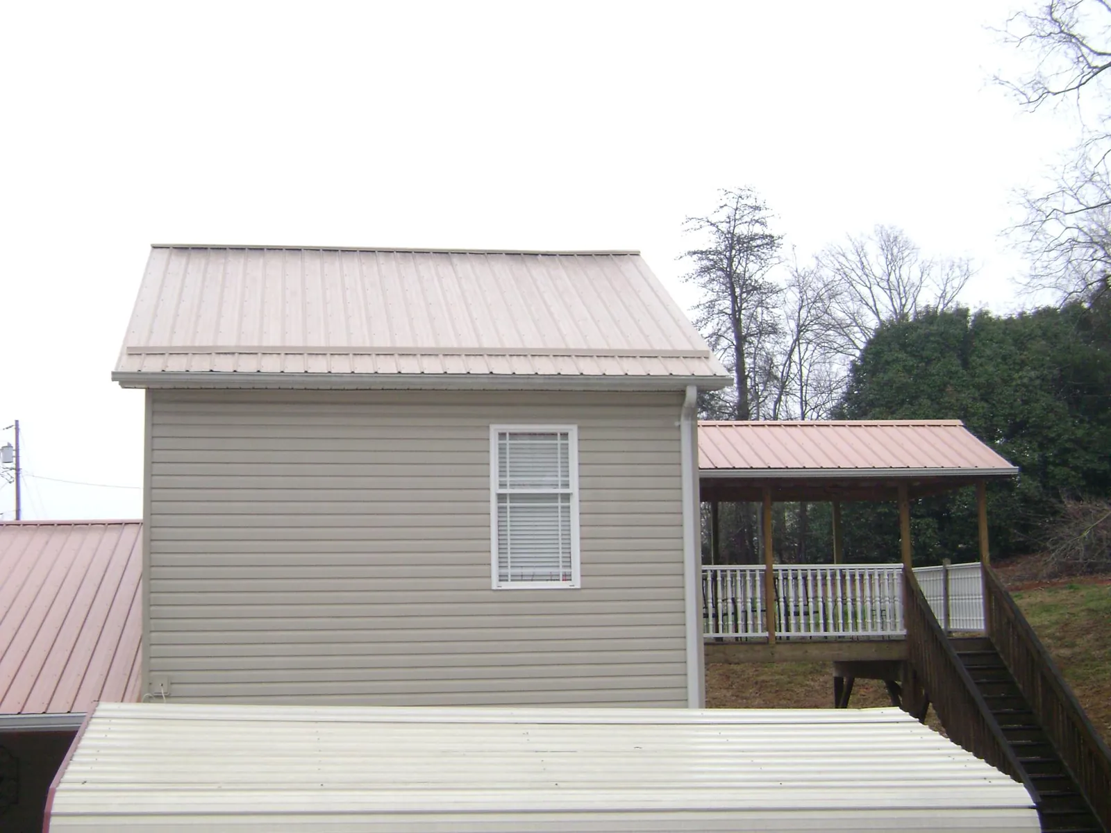 Tan metal roofs on a two story addition and attached porch, from a Roof Replacement job in Rensselaerville